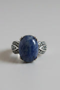 A silver ring featuring an oval blue stone with natural marbling, set on a light gray background.